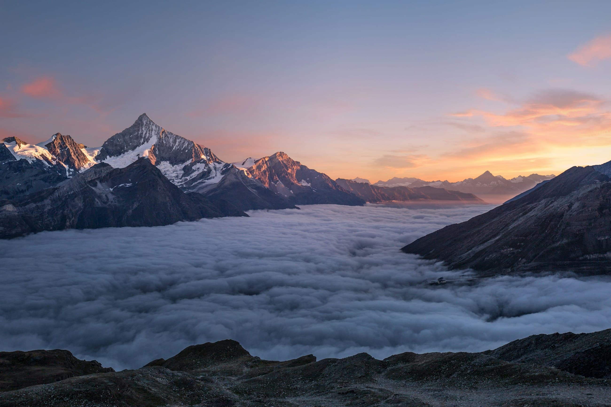 A mountain summit rising above a sea of clouds at sunrise.